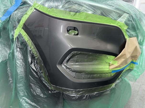 Lackierung am Fahrzeug Abgeklebte graue Stoßfängerecke während der Lackierarbeit am Fahrzeug