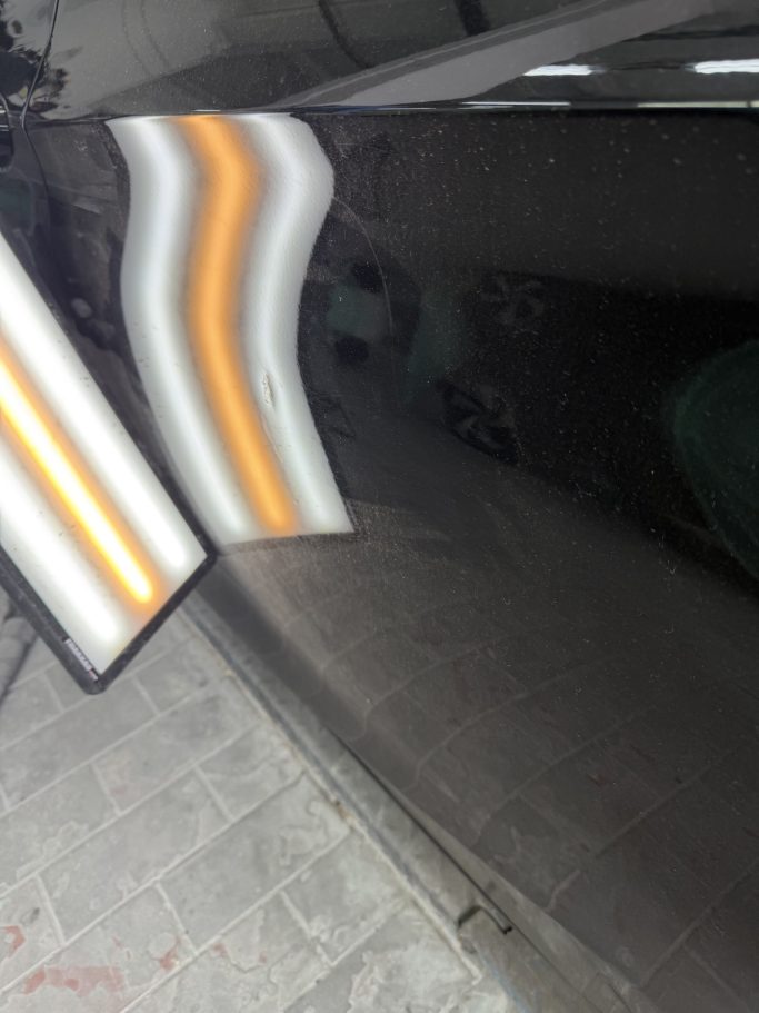 Delle an einer schwarzen Fahrzeugtür unter einer Kontrollleuchte