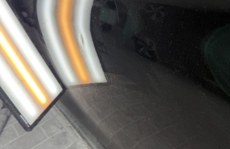 Dellenentfernung ohne Lackieren Delle an einer schwarzen Fahrzeugtür unter einer Kontrollleuchte