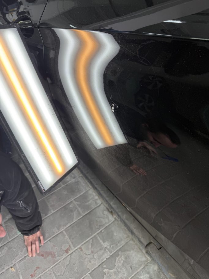 Schwarze Fahrzeugtür mit gespiegelten Lichtstreifen aus einem zweiten Blickwinkel